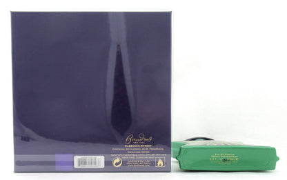 A dark purple rectangular box with gold lettering and a barcode, shown next to a green rectangular item on a plain white background.