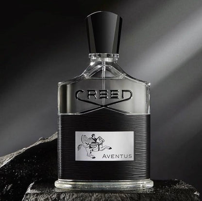 Creed Aventus perfume bottle with a black cap and a black-and-silver textured body, displayed on a dark stone surface against a dramatic dark gray background.
