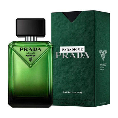 Prada Paradigme Milano Eau de Parfum bottle in green glass next to its textured dark green packaging box on a white background.