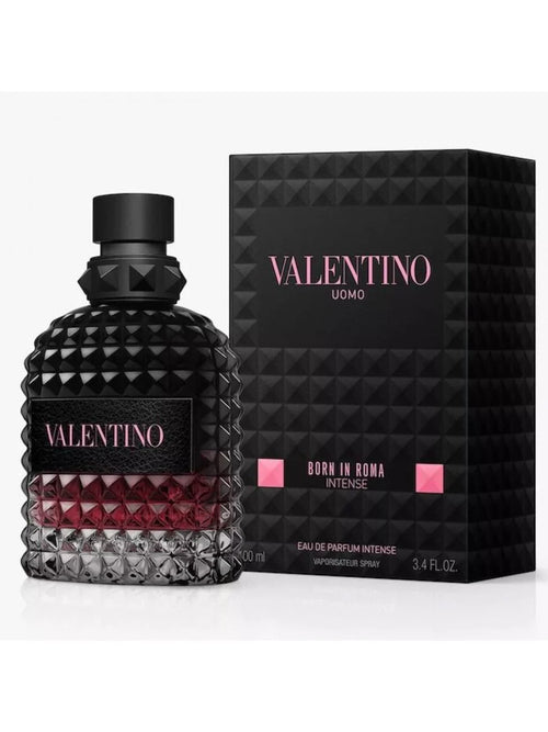 Valentino Uomo Born in Roma Intense Eau de Parfum Intense bottle with a textured black cap and base, showing a deep red liquid inside, next to its black geometric packaging box with pink lettering.
